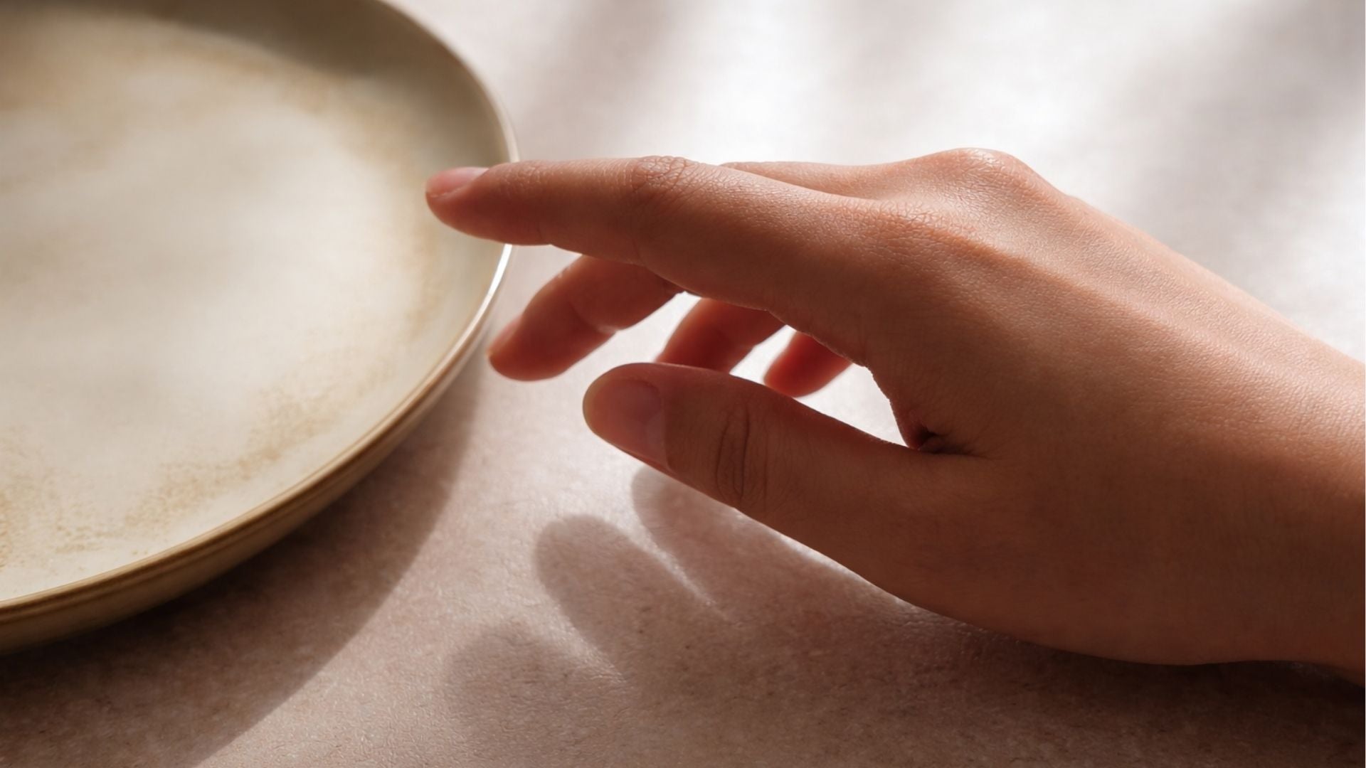 Hand reaching towards a ceramic plate on a textured surface